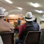 Photographed from behind are 3 cowboys sitting beside one another.