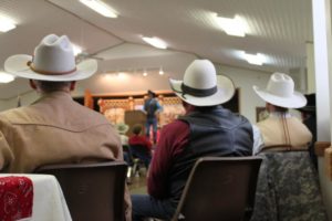 Photographed from behind are 3 cowboys sitting beside one another.