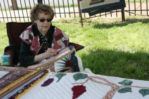 Lois Mueller hand stitching in a folding chair.