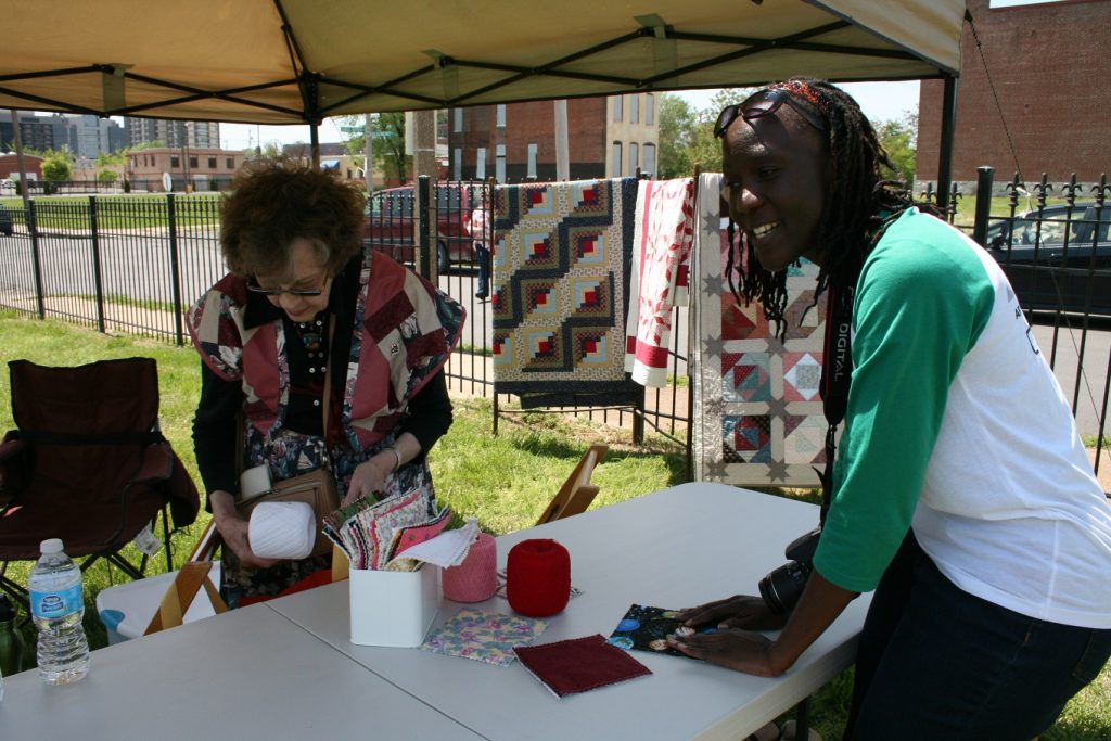 Lois Mueller searches for the thread that graduate student Dorothy Athuhura should use. Between the two are threads and various quilt patches.