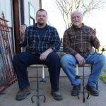 Photo of apprentice Matt Dickson and master blacksmith Bob Alexander sitting outside Scrub Oak Forge holding lamps.