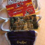 Custom made face mask by quilter Patti Tappel. Mask one is a cherry print, 2 is the Kansas City Chiefs logo. Mask 3 is a camoflauge mask with a brown bear, and mask 4 is a purple mask with the Crown Royal logo.