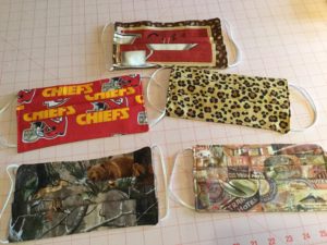 Custom masks by Patti Tappel. Mask one is a coffee mask with red background, two is the Kansas City chiefs logo. Mask three is a cheetah print, four is a camo with brown bear, and five is a collection of postcards collaged together.