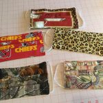 Custom masks by Patti Tappel. Mask one is a coffee mask with red background, two is the Kansas City chiefs logo. Mask three is a cheetah print, four is a camo with brown bear, and five is a collection of postcards collaged together.