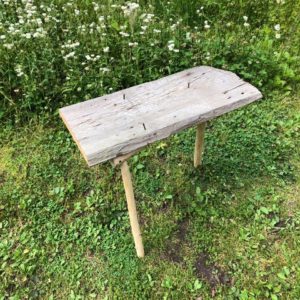 An almost finished wooden school, courtesy of James Price, master woodworker. Price has created a V shaped wooden based to the stool with 3 legs and hammered the wooden seat onto the frame using old square nails. This is a near finished product.