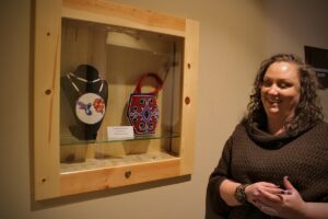 Woman stands in front of gallery cases of two beaded works.