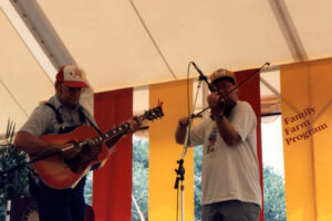 Guitarist on left accompanies fiddler on right on a stage with red and yellow bunting decorating the stage.