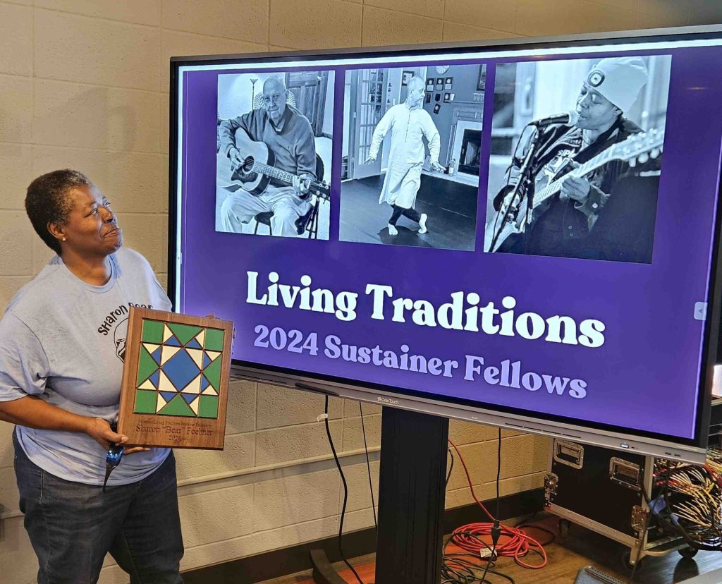 Sharon Foehner poses with her fellowship plaque in front of a screen depicting the 2024 fellows