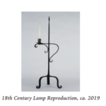 A black metal three-legged, table top lamp with a candle