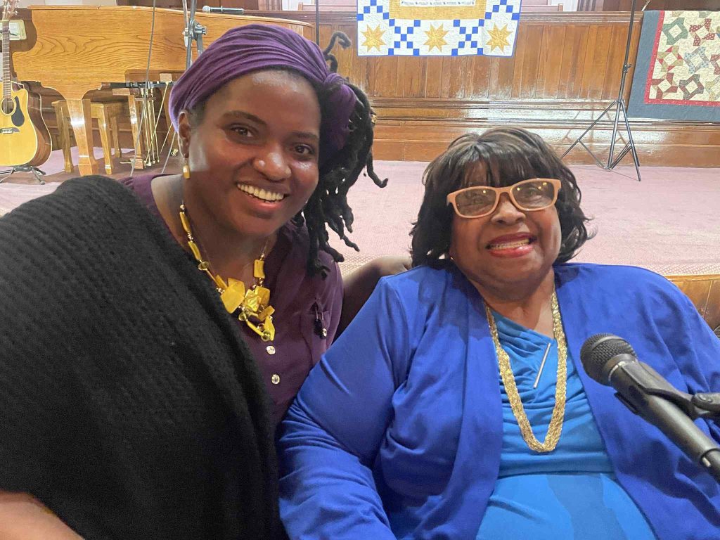 Angela Williams on the left sits next to Gladys Caines Coggswell in front of a mic.
