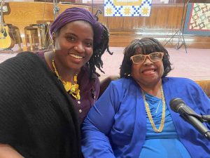 Angela Williams on the left sits next to Gladys Caines Coggswell in front of a mic.