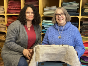 Two women posed in front of shelves of wool fabric