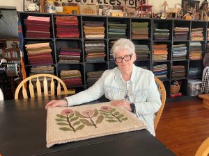 Women sits at table with floral textile on table.