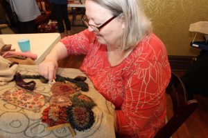Woman in red blouse hooks floral rug.