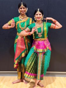 Two women in bright dresses exhibit hand gestures of Indian dance traditions.  